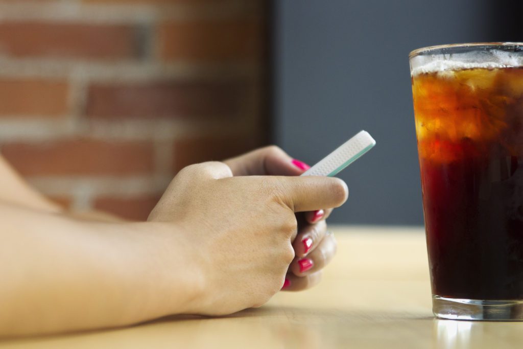 A person is holding their cell phone in one hand and drinking soda.