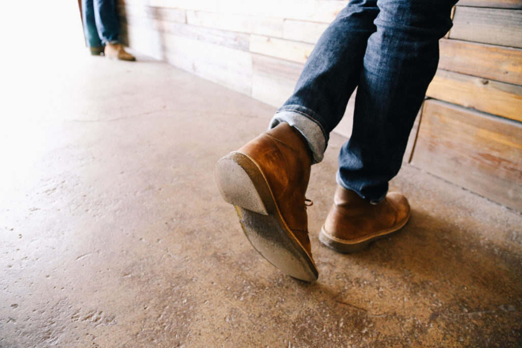 A person wearing brown shoes and jeans standing on the ground.