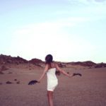 A woman in white dress standing on top of a sandy beach.