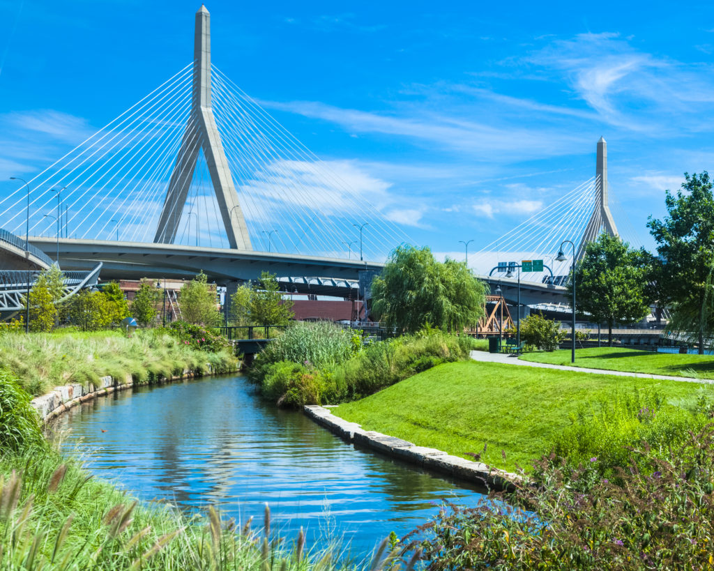 A bridge over water with grass and trees in the foreground.