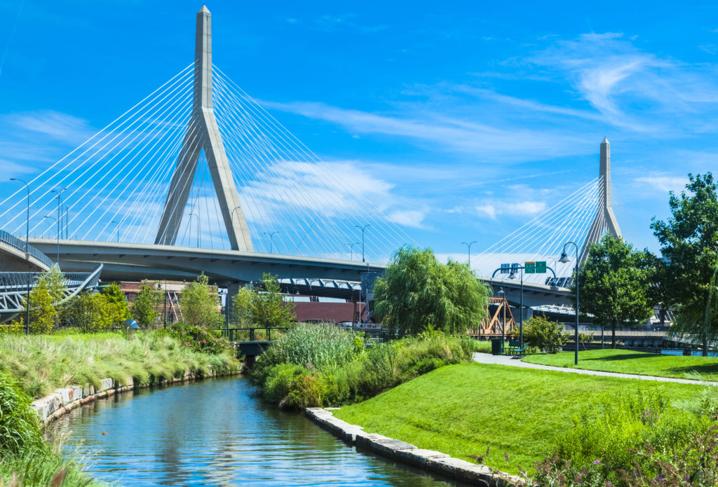 A bridge over water with trees and grass in the foreground.