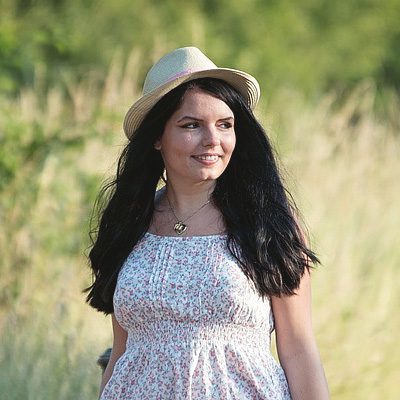 A woman in white dress and hat standing next to grass.