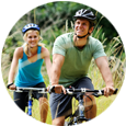 A man and woman riding bikes through the grass.