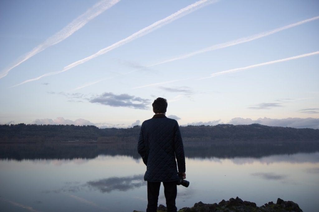 A man standing in front of the water holding a camera.